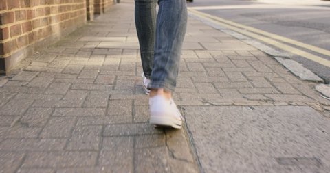 Detail of woman's feet walking through city on pavement from behind