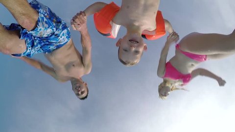 SLOW MOTION CLOSE UP: Young parents and their cute son child jumping over the camera into pool splashing around