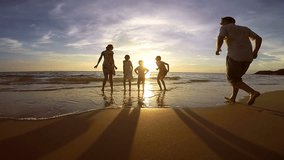 Silhouette of happy people who playing on the beach at the sunset time. Concept of friendly family. Video filmed on camera Gopro.