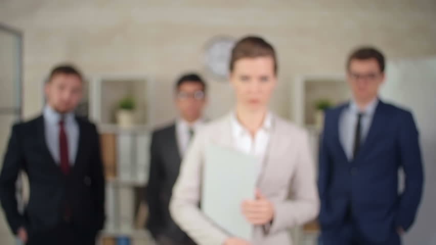 Camera focusing on self-confident female business leader, her team standing behind her 