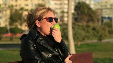 Portrait of a woman sitting on a park bench and eating green apple