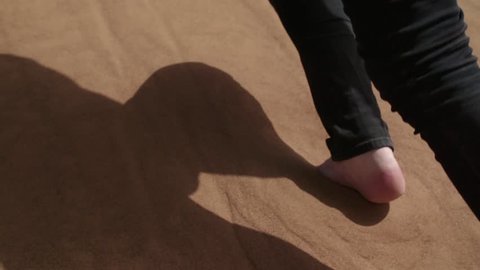 Bare feet climbing a sand dune in slow motion