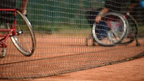 Wheelchair tennis player is seen behind the tennis net on a clay court