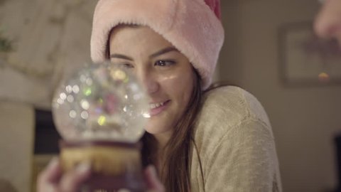 Teen Flips A Snow Globe For Her Friend, Closeup Of Multiethnic Teen, Wearing Santa Hat, Watching Snow Fall ஸ்டாக் வீடியோ