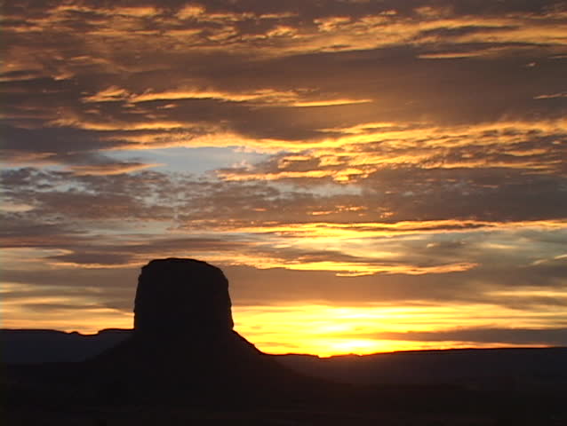 A butte stands in silhouette beneath golden clouds in Monument Valley.
