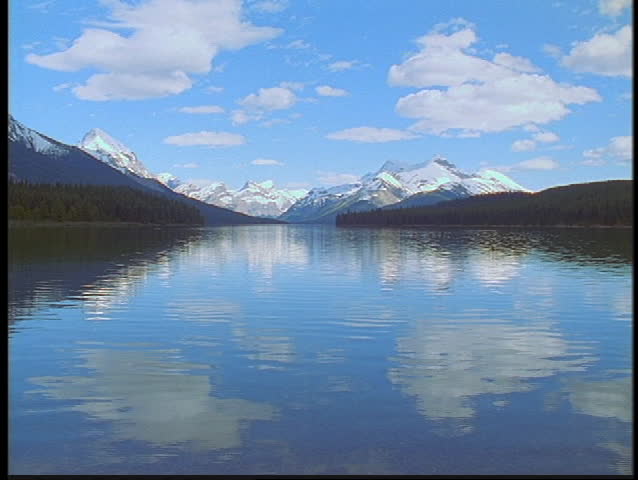 The Canadian Rockies and clouds reflect in a lake.