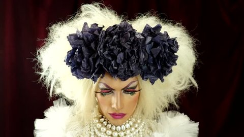Drag queen with a glamorous and spectacular look opening eyes and posing using hands