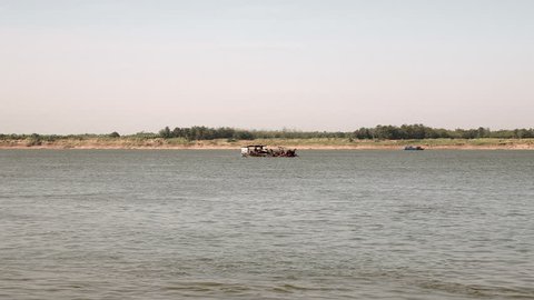 Dredging boat going down the river filled with riverbed sand (distance view)