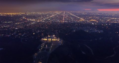 Aerial view of illuminated Los Angeles cityscape at night with Griffith Observatory in foreground. 4K UHD.