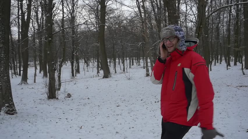 Man is Talking by Mobile Phone And Smiling, slow motion, Walking Around a Camera, Happy Young Man, Smiling Man in Glasses, Man with Short Beard in Red Sporty Jacket and Fur Ear Flaps Hat, Ushanka,