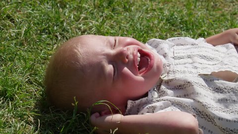 A crying boy lying on grass tries to tear his shirt off. 4k. Slow motion.
