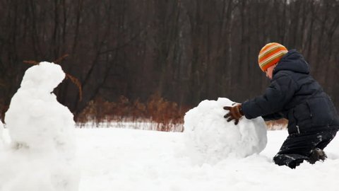 little boy rolls big snow ball for snowman in winter