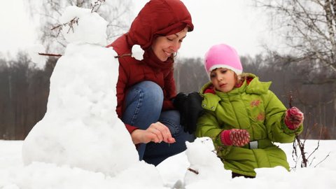 mother with cute little daughter make face for small snowman