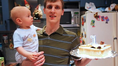 little baby in fathers hands try catch birthday cake on one year old