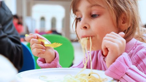 small pretty girl with yellow fork in hands eats pasta, close-up