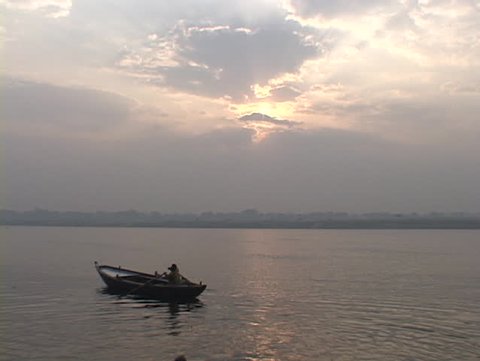 A man rows a boat against a pale sky on the Ganges River.