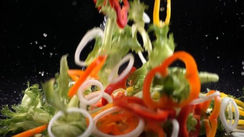fresh vegetables falling with water on black background in slow motion