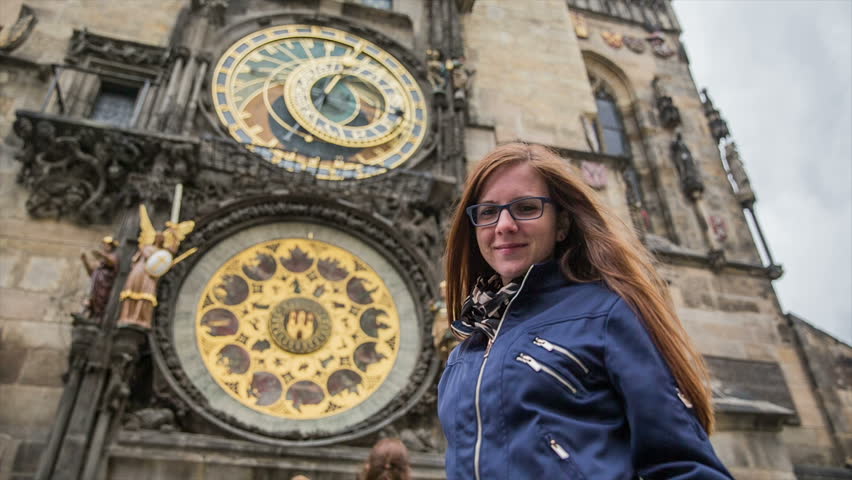 Woman portrait shot in front Prague astronomical clock. Low angle view of attractive female person with long brown hair blowing in windy Prague with astronomical clock in background.