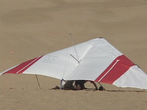 A hang-glider falls into the sand after an unsuccessful trial run.