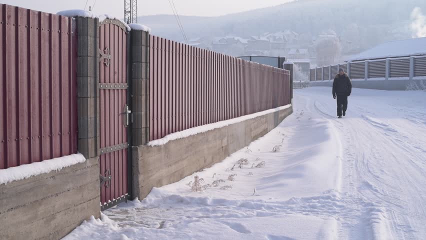 Man is walking along the fence and knocking at the door. Nobody replies and he goes away.