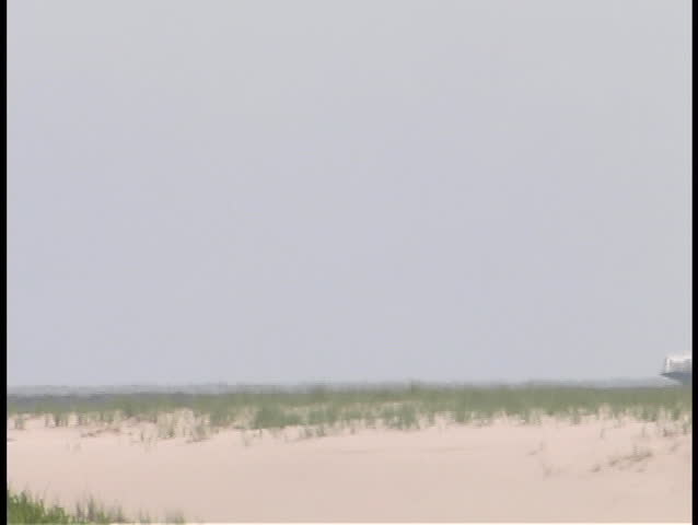 A passenger boat passes by a sandy coastline.