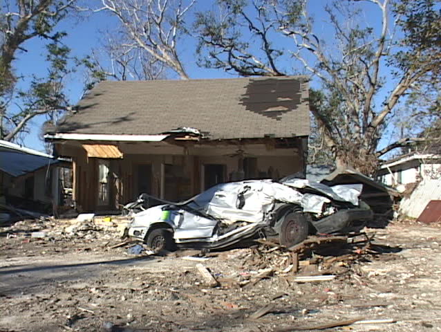 A crushed car in front of a home shows the destruction caused by Hurricane Katrina. | Shutterstock HD Video #1400551
