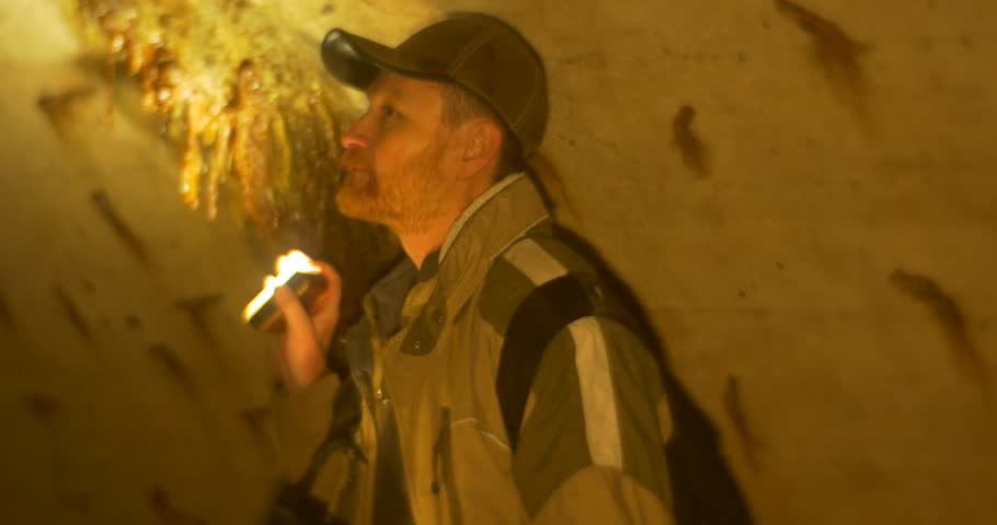 Tourist, Man is Observing Carefully a Cave Walls, Stalactites on a Wall and Water that Drips from a Stalactites, Man with Beard Lights the Wall by a Lamp, Looking Attentively, Man in Cap, Backpacker,