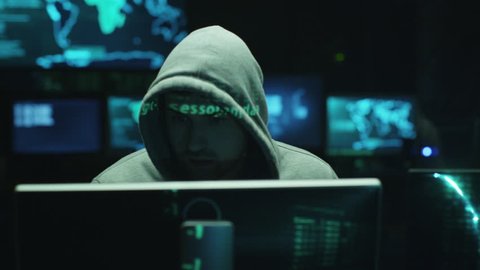 Male hacker working on a computer while green code characters reflect on his face in a dark office room. Shot on RED Cinema Camera in 4K (UHD).