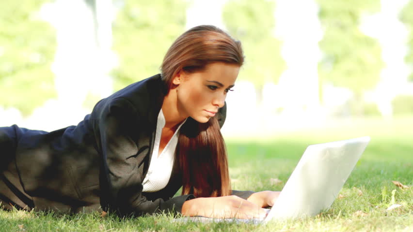 Beautiful business woman laying on grass and using laptop