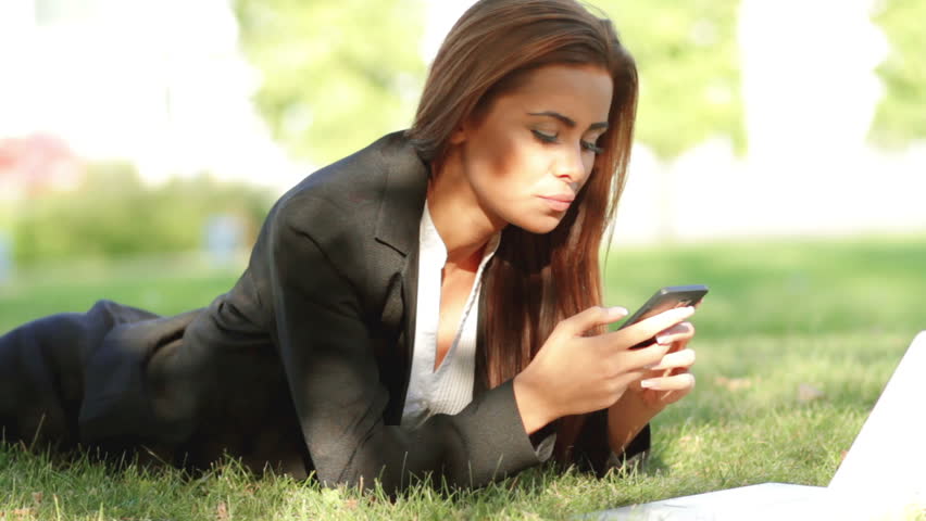 Beautiful business woman relaxing on grass with laptop and phone
