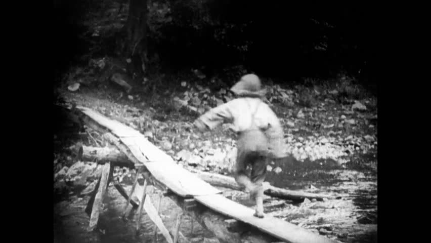 Rear view of boy running on footbridge across river, 1920s