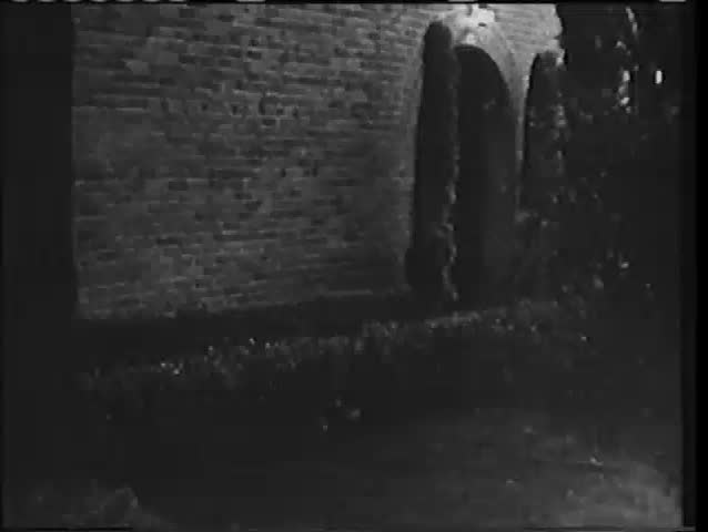 Rear view of woman cautiously entering brick building, 1940s