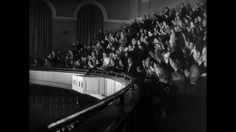 Side view of audience in balcony fervently applauding, 1940s