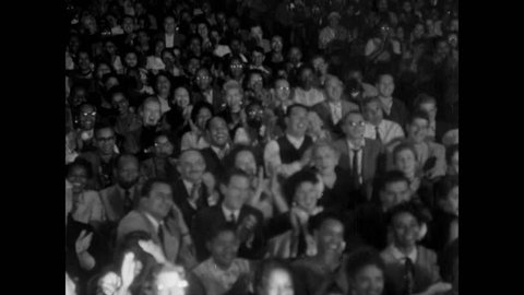 Audience applauding in theater as spotlight pans from left to right , 1950s