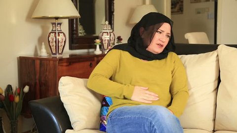 Sick muslim woman sitting on a sofa and having abdominal pain