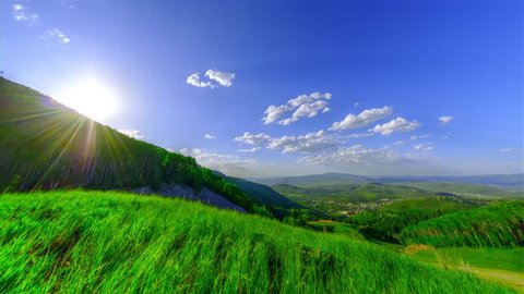Sun is shining through mountain and field of grass.