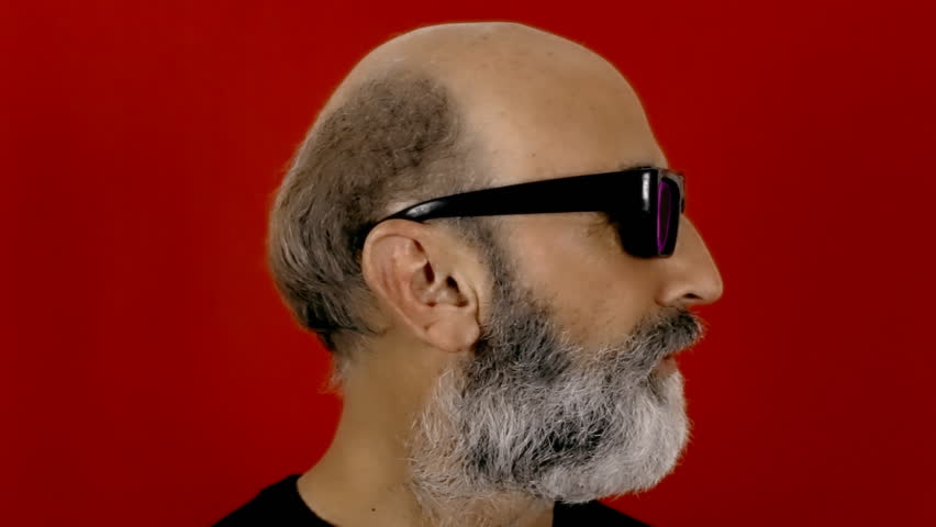 An old man with hypnotic glasses reflecting a big fire on a dark night. Close-up shot, red background.
