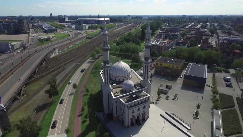 Aerial footage from the south side of Rotterdam, Netherlands in Europe. Circling around a mosque with De Kuip, the River Maas and the city skyline with skyscrapers in the background.