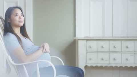 Pregnant asian woman in rocking chair holding belly