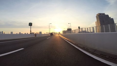 Driver's point of view across the bridge towards the climbing sunshine over the city horizon. Part 3. Eastbound over the Rainbow Bridge towards Daiba.