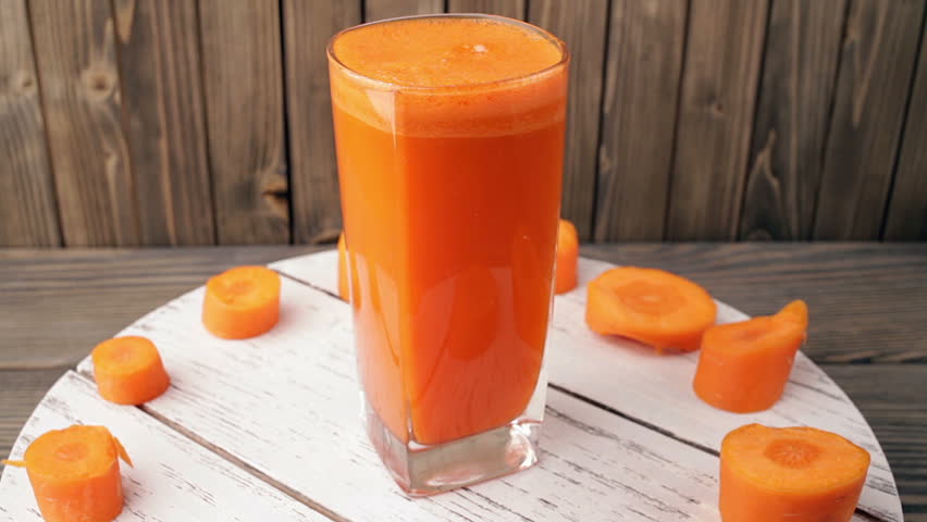 carrot juice into glass  rotating, wood background. Seamless Loop