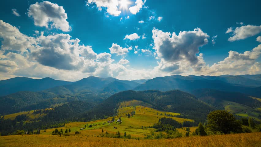 Timelapse of clouds passing by summer landscape with bright sun in blue sky and mountains in the background