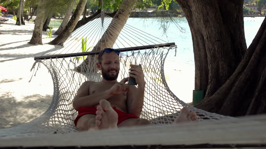 Young man relaxing while lying on hammock on the beach

