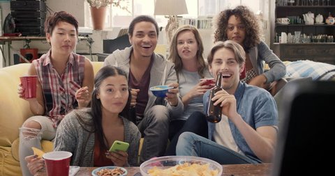 Happy diverse group of student sports fans throwing arms up in excitement celebrating goal watching sports event on TV together bonding as friends eating snacks drinking beer