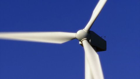 Close up of a brilliant white wind energy turbine turning against a clear blue sky.