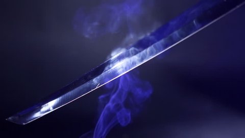 Japanese katana sword. Blade close-up on a dark background with blue light filter with incense smoke. Steel tempering