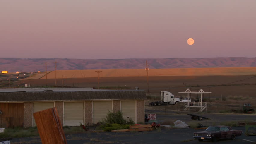 Large moon rises over colorful hills in small town