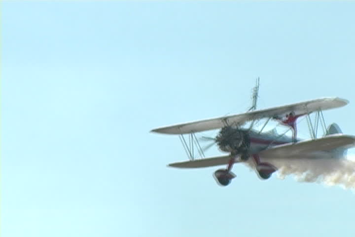 Woman performs stunts on the wing of a vintage airplane high in the sky.