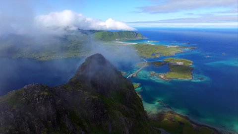 Scenic flight over cloudy mountain peak with amazing view of bridges connecting islands deep down below. Aerial 4k Ultra HD.
