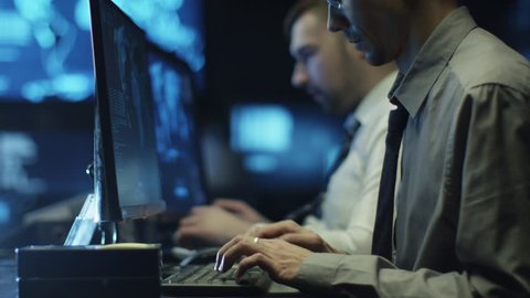 Two IT programmers are working on computer in a dark office room filled with display screens. Shot on RED Cinema Camera in 4K (UHD).
